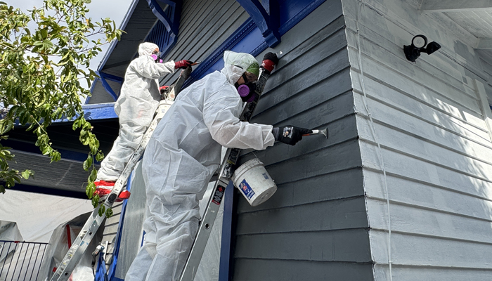 Lead remediation workers in protective suits repairing a home exterior.