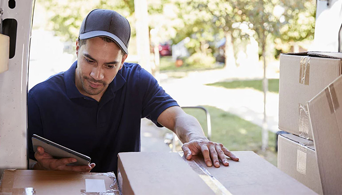 Delivery worker reviewing a tablet while handling shipping boxes
